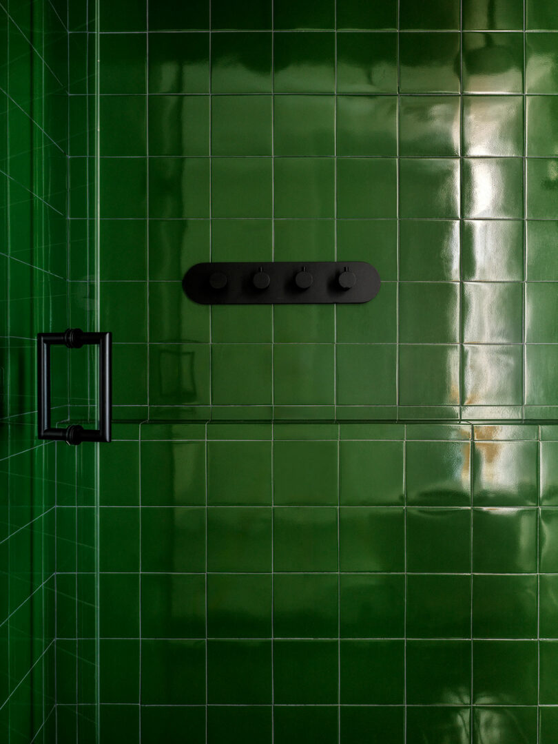 Shower with glossy dark green tiles and matte black fixtures, including a row of four knobs and a handle on the door.