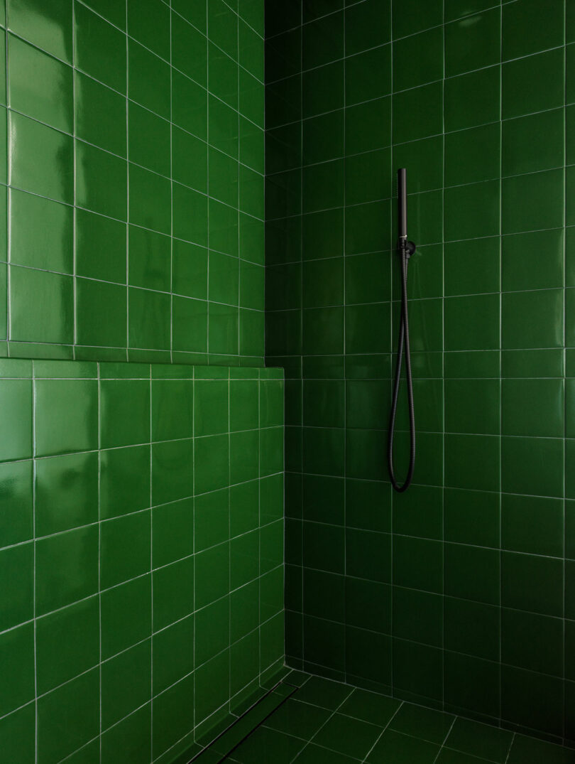 A minimalist shower area with bright green tiled walls and floor, featuring a sleek black shower fixture.