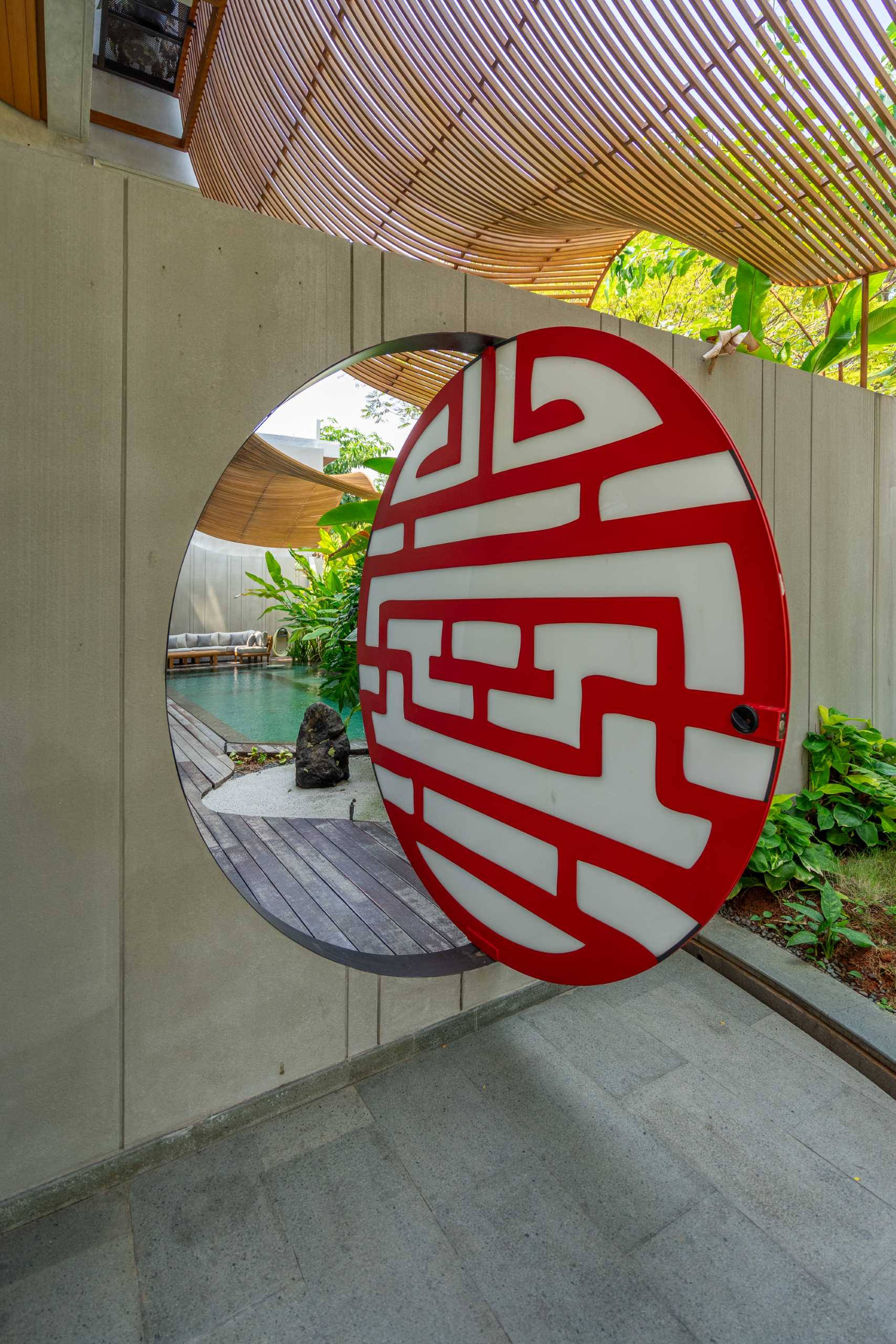 The shaded entryway of this home home includes a circular opening that provides a glimpse of the pool on the other side of the wall.