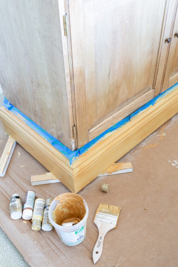 Using paint to create a faux wood finish on the bottom trim of a wood cabinet.