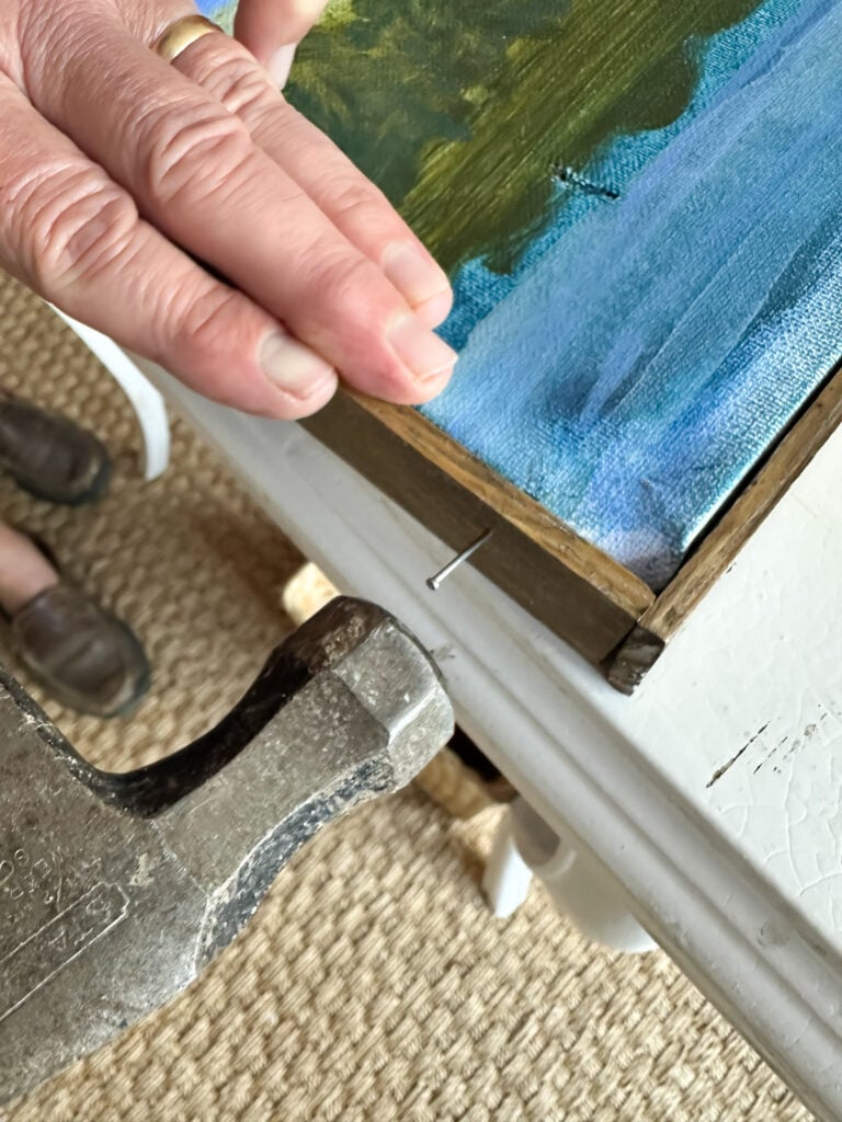 hammering in a nail to attach wood frame to art canvas