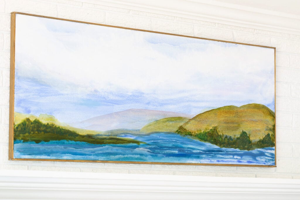 Finished, framed and hung on wall painted art canvas with a water and mountain scene.
