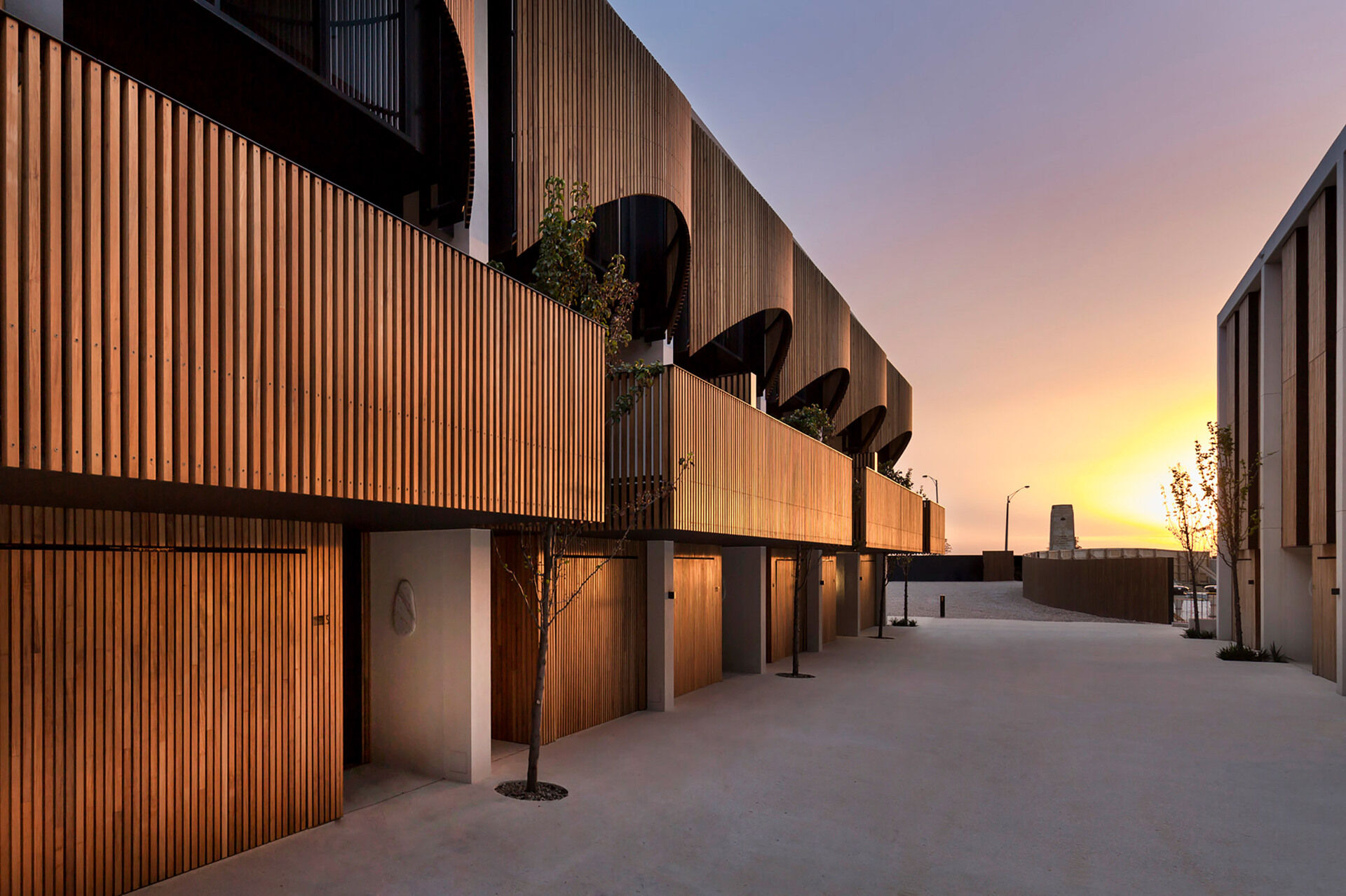 Along a tree-lined shared path, these townhouses feature softly fluted timber screens, overhanging terraces, and a warm, finely detailed palette that adds intimacy and rhythm to the streetscape.
