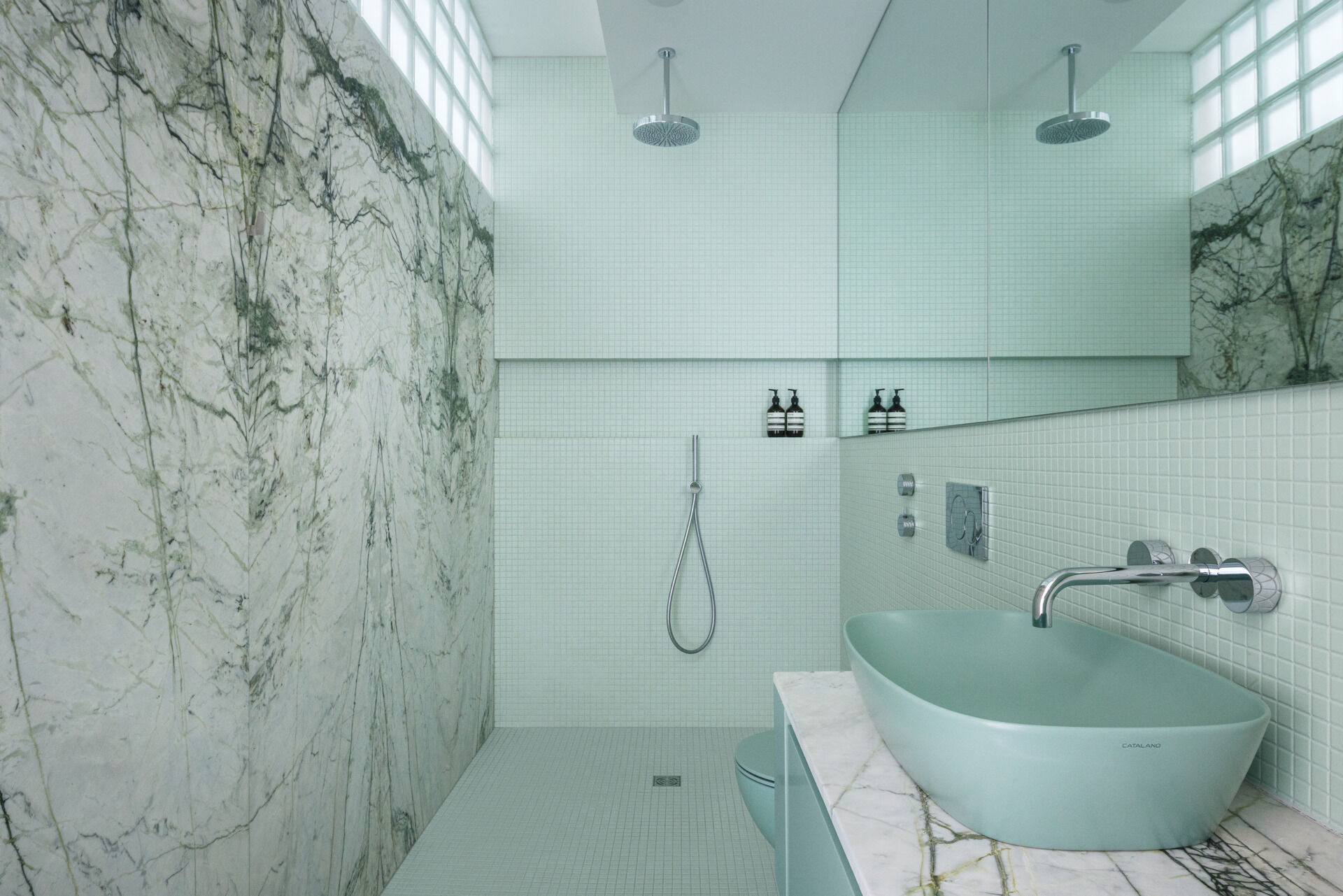 Calacatta verde marble, soft tile, and retro glass blocks bring luxury and light into this modern Montreal bathroom with timeless flair.