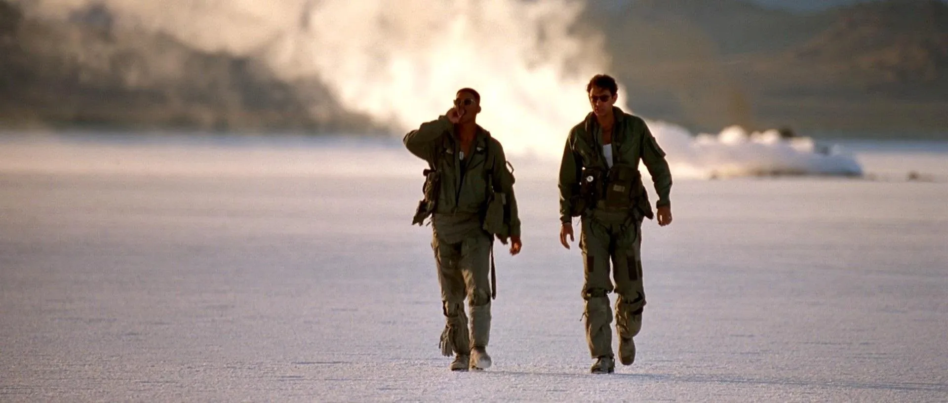 Two military personnel walking across a desert landscape.