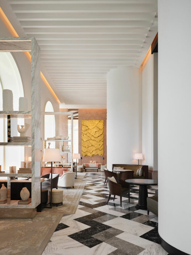 Modern hotel lobby with high ceilings, marble floors in a geometric pattern, white walls, contemporary furniture, and a large textured yellow artwork on the far wall inspired by Dorothée Boissier’s elegant style.