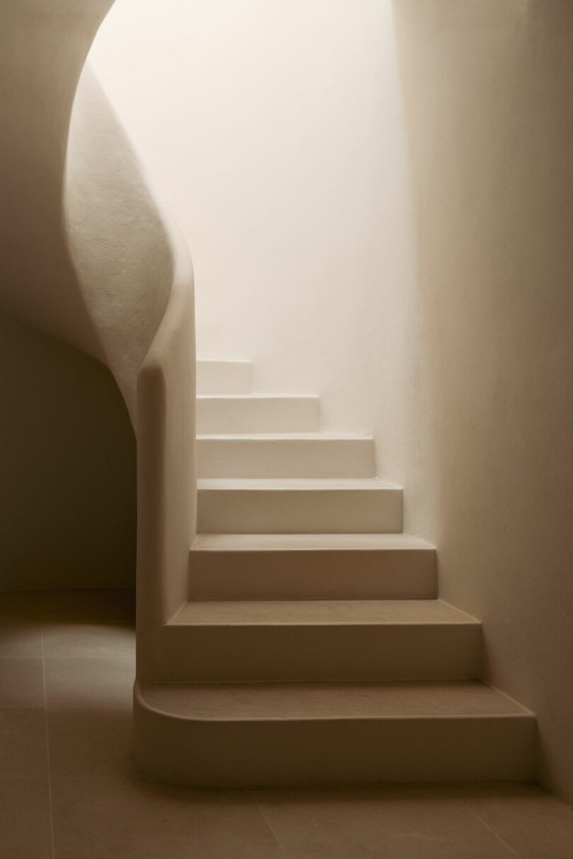 Minimalist, curved staircase with smooth, beige plaster walls and soft natural light illuminating the steps from above.