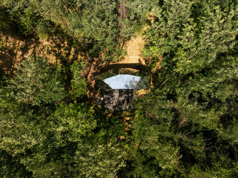 An aerial view of a mirrored building surrounded by dense green trees, blending into the forest environment.