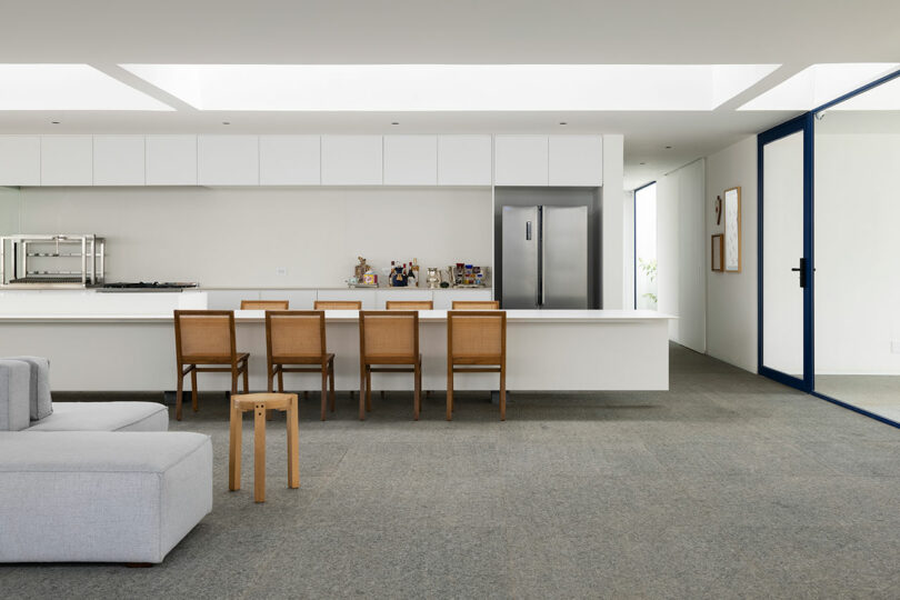 interior view of minimalist white kitchen with long island and wood chairs