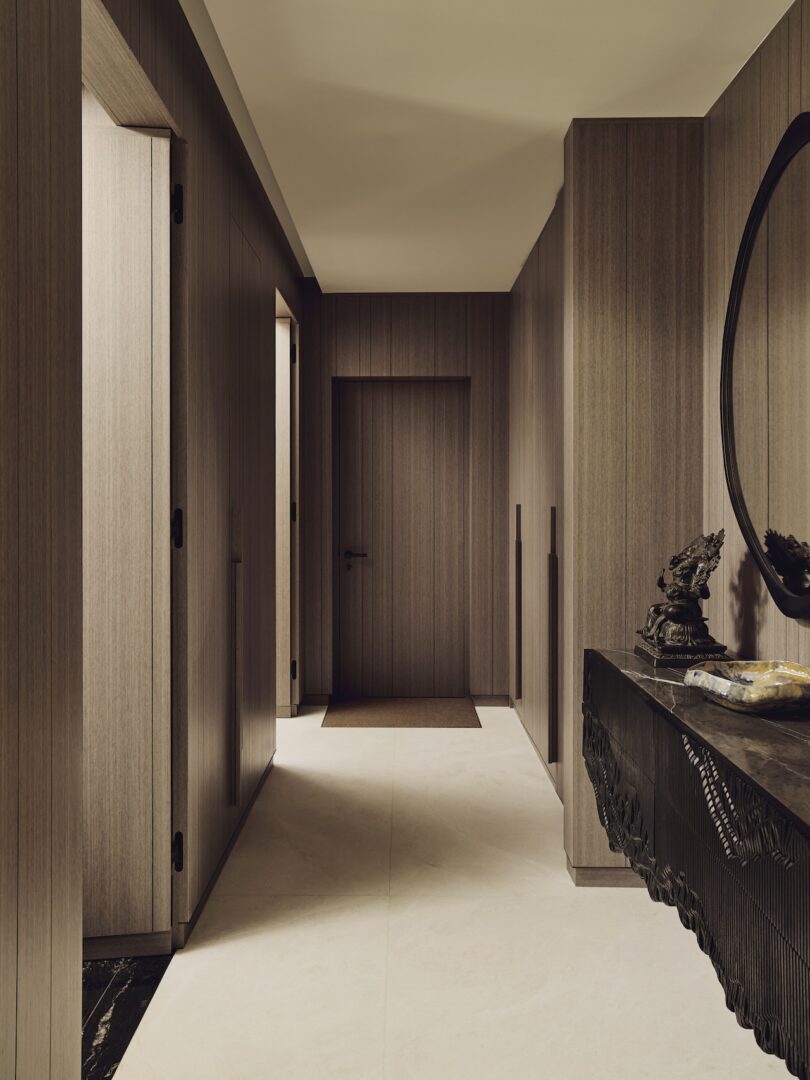 A modern hallway with wood-paneled walls, a closed door at the end, and a dark console table with decorative objects on the right side.
