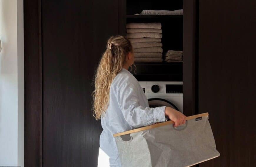 a woman carrying a laundry bag, facing a cabinet with hidden washer dryer
