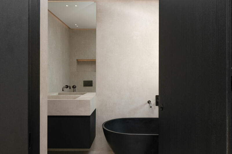 Minimalist bathroom with beige walls, a rectangular sink and countertop, black cabinet, black wall-mounted fixtures, and a black freestanding oval bathtub.