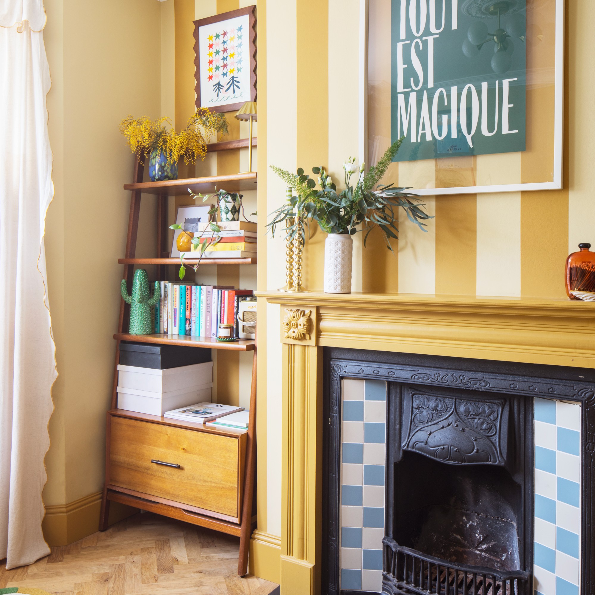 A yellow living room with a striped wall and a midcentury-style bookcase in an alcove displaying books and decor