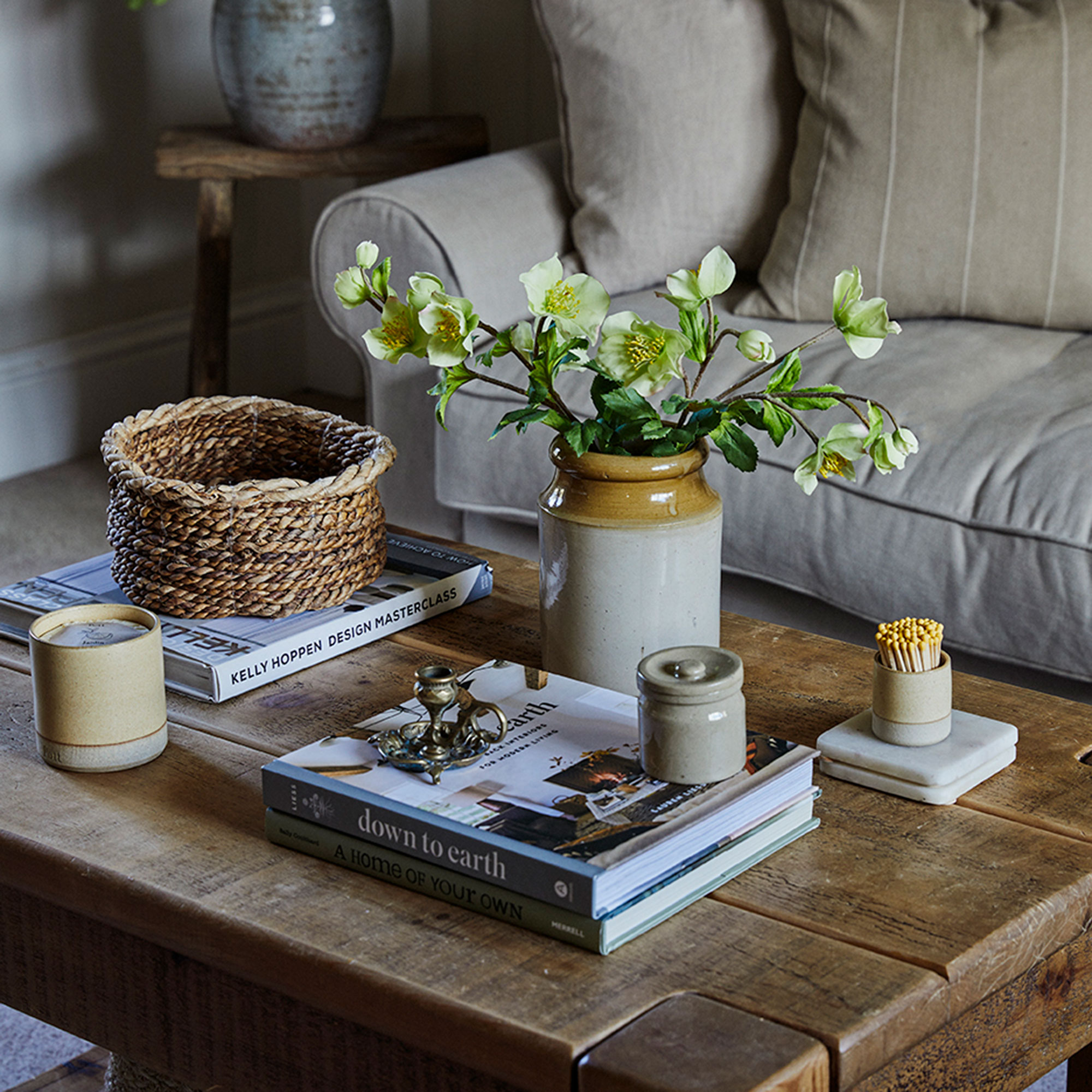 Wooden coffee table with books stacked on top and earthenware vase and candle
